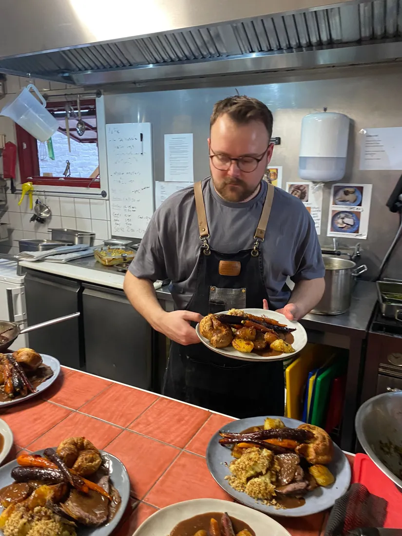 Ben in a chef apron plating Sunday roasts
